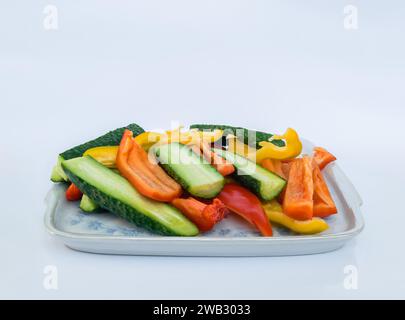 Vegetable slices of yellow and red peppers and cucumbers on a square shaped porcelain dish with rounded corners on a white background Stock Photo