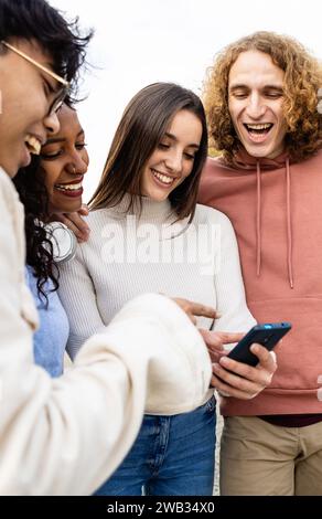 Happy diverse friends laughing while watching funny videos on smartphone Stock Photo