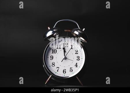 Close-up of a retro alarm clock face on a black background. Clock hands move fast, the beginning of time 12:00 AM or 12:00 PM. Stock Photo