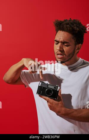 young african american man looking at his vintage camera on red background, pushing button Stock Photo