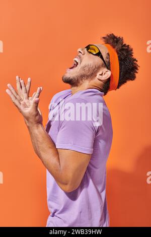 expressive african american man in eyeglasses and headband screaming on orange background Stock Photo