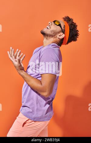 expressive african american man in eyeglasses and headband screaming on orange background, gesture Stock Photo