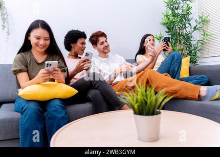 Diverse friends smiling and using smartphones on a sofa, enjoying tech interaction.  Stock Photo