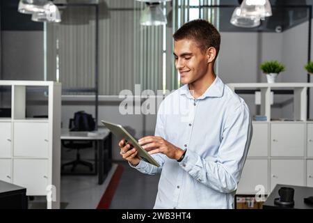 Young handsome businessman using digital tablet while standing in the office Stock Photo