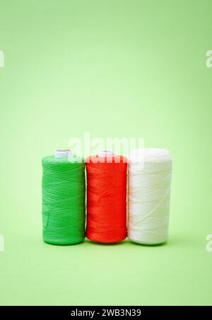 Various spools of sewing cotton thread of different colors italian flag on green background Stock Photo