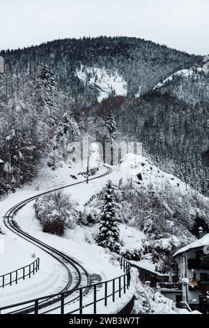Snowy Wonderland: Rooftops, Alpine Peaks, and Uphill Railway Tracks in Austrian Splendor. Stock Photo