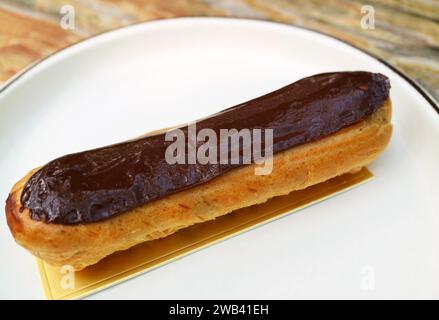 Closeup of Delectable Chocolate Eclair on a White Plate Stock Photo