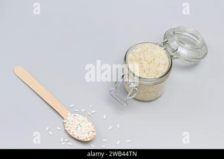 Three types of white rice in glass jar, wooden spoon and bowl. Top view. Gray background Stock Photo