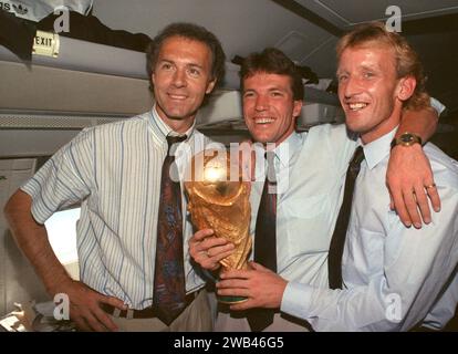 FILED - 09 July 1990, Italy, Rom: On the plane returning from Rome to Frankfurt, former DFB team manager Franz Beckenbauer (l), captain and midfielder Lothar Matthäus (M) and defender Andreas Brehme, who scored the decisive goal, present the World Cup trophy. Franz Beckenbauer is dead. The German soccer legend died on Sunday at the age of 78, his family told the German Press Agency on Monday. Photo: Wolfgang Eilmes/dpa Stock Photo