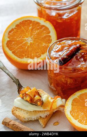 A jar of homemade orange jam with cut orange fruits, cinnamon stick and rustic tea spoon Stock Photo