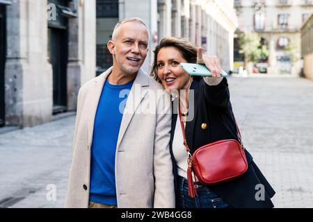 Carefree middle aged couple looking for touristic location pointing and holding smartphone. Happy senior man and woman sightseeing and exploring a Stock Photo