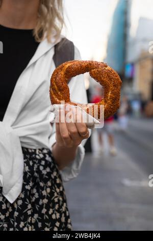 Woman holds a close-up of a traditional Turkish bagel Simit on the street. Turkish fast food. Vertical photo Stock Photo