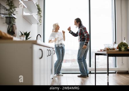 Old couple spends free time dancing twist in modern light kitchen Stock Photo