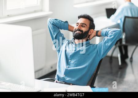 Relaxed indian male office worker leaning back in his chair, smiling Stock Photo