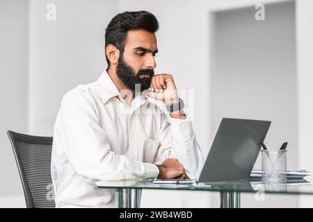 Indian businessman in deep thought at laptop in modern office Stock Photo