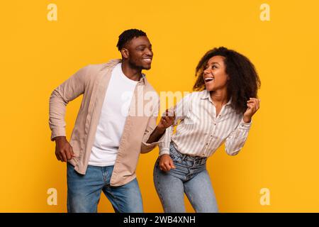 Cheerful African American couple dancing and laughing together on yellow backdrop Stock Photo