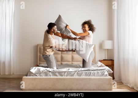 African American couple having playful pillow fight, flirting in bedroom Stock Photo
