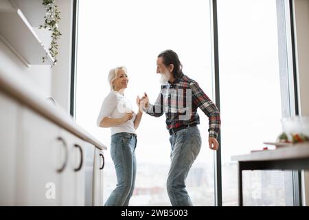 Old couple spends free time dancing twist in modern light kitchen Stock Photo