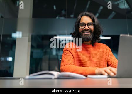 Smiling young indian businessman sitting at worktable at modern office Stock Photo