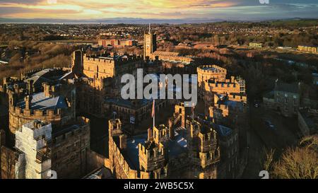 Aerial view of a historic castle at sunset with surrounding landscape and town under a golden sky in Lancaster. Stock Photo