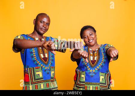 Smiling black couple showing thumbs down gesture and looking at camera. Cheerful african american man and woman showcasing disapproval sign, giving negative feedback studio portrait Stock Photo