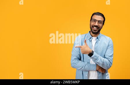 A charismatic man with a beard and glasses smiles and points sideways with his left hand Stock Photo