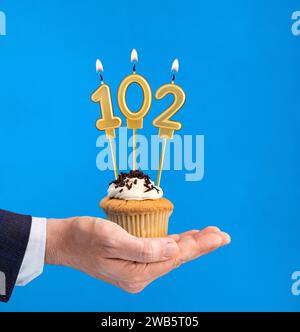 Hand delivering birthday cupcake - Candle number 102 on blue background Stock Photo