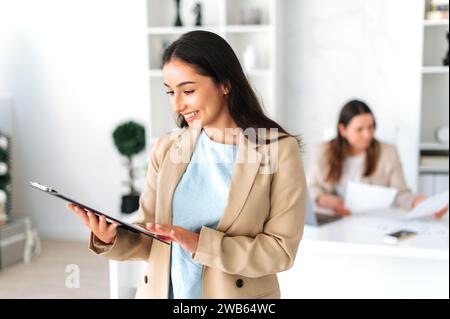 Positive successful confident indian or arabian business woman, secretary, company executive, financial advisor standing in the modern office, studying documents, smiling Stock Photo