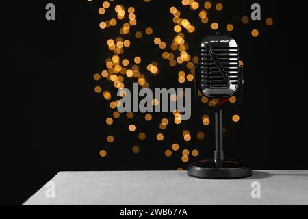 Vintage microphone on table against black background with blurred lights, space for text. Sound recording and reinforcement Stock Photo