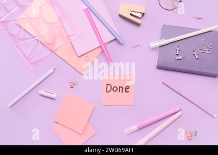 Sticky note with word DONE and stationery on lilac background Stock Photo