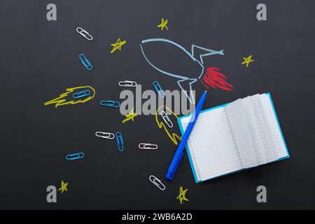 Creative composition with drawn rocket and different stationery on black chalkboard Stock Photo