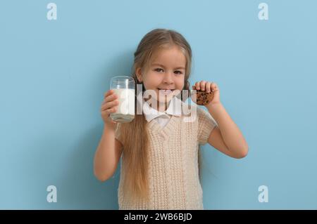 Cute little girl with glass of tasty milk and cookie on blue background Stock Photo