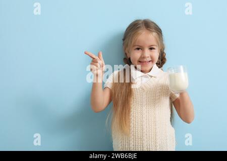 Cute little girl with glass of tasty milk pointing at something on blue background Stock Photo