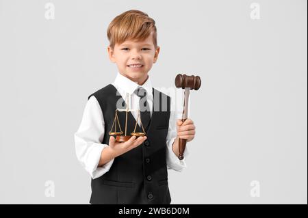 Cute little judge with gavel and justice scales on light background. Opposite Day celebration Stock Photo
