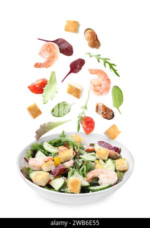 Ingredients falling into plate with tasty salad on white background Stock Photo