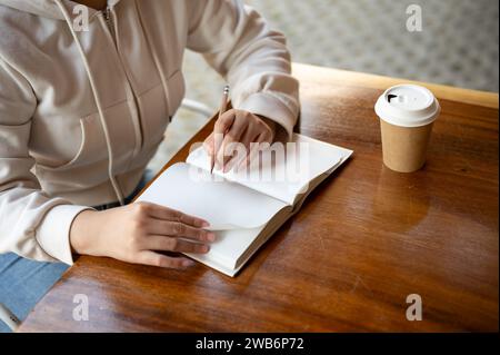 Cropped image of a woman writing something in a book at a table in a cafe. keeping diary, making notes, making lists, doing homework Stock Photo