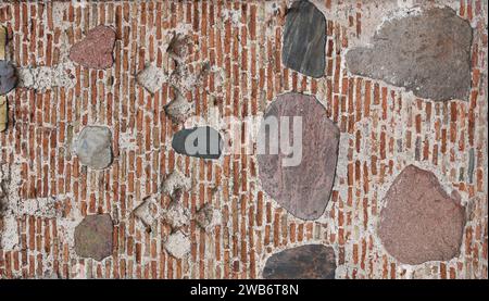 Abstract background from a wall with bricks and stones. Old fortress wall of red brick interspersed with large cobblestones Stock Photo