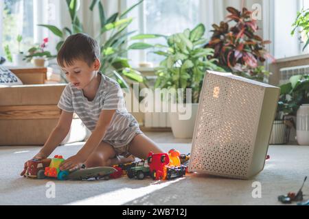 A cheerful European boy plays with cars on the carpet in his room.  Stock Photo