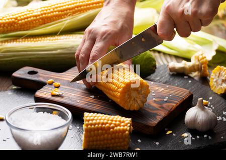 Female hands cut sweetcorn cobs on cutting board low angle view Stock Photo