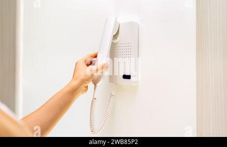 Intercom handset in female hand. Intercom on white wall with copy space. Stock Photo