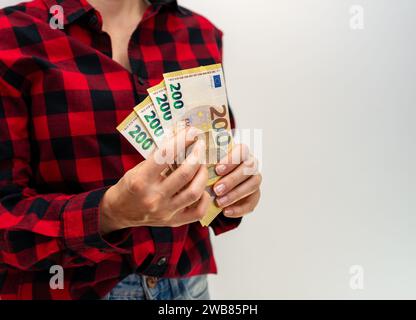 Unrecognisable female person in red casual shirt holds money in hands, 200 euro banknotes in hands. Stock Photo