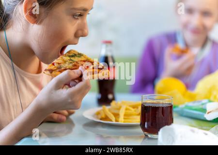A happy little girl in a restaurant. A child Eating pizza with his mouth open with a cola in his hands. Stock Photo