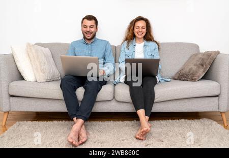 Young couple sitting on sofa at home and uses laptops. Online shopping, booking, banking. Stock Photo