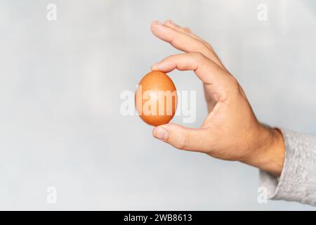 Young hand holding raw egg over blue background. Stock Photo