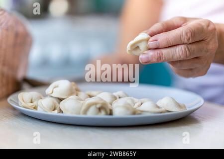 sculpt dumplings by hand with hands in flour. an old elderly woman holds molded dumplings in her hand. Stock Photo