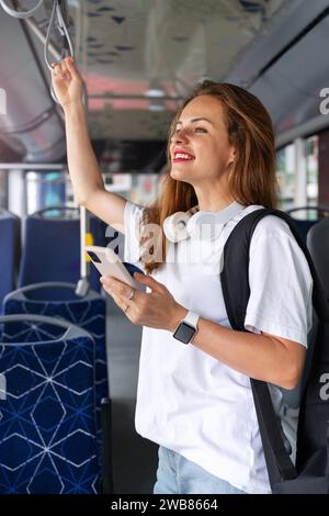 Young urban woman with smart phone stands on the bus. Passenger and city transportation City life. Stock Photo