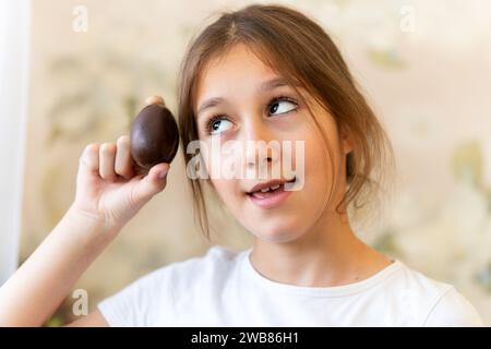 A child opens a chocolate egg. The girl is surprised by the surprise. The child girl holds a chocolate egg in her hands and looks forward to a good su Stock Photo