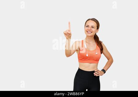 Woman wearing sportswear touching virtual display with her finger choosing workout exercise, nutrition, sports product. Stock Photo