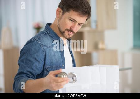 young handsome man hanging window curtain in room Stock Photo