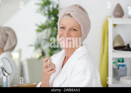 cheerful senior woman applying perfume after her shower Stock Photo